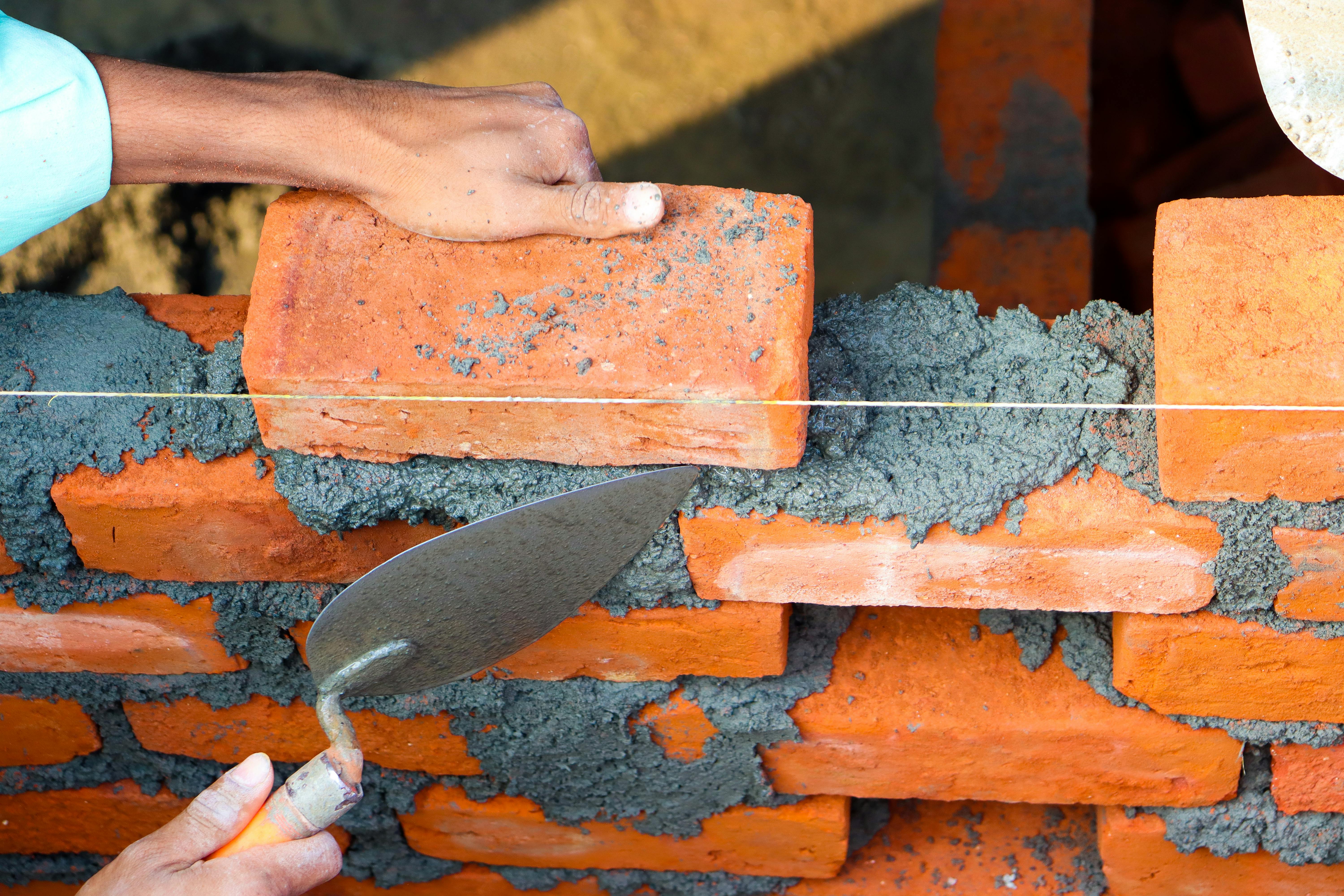 A hand lays red bricks to build a wall with gray mortar, a methaphor for what you can build when you start small and stay consistent.