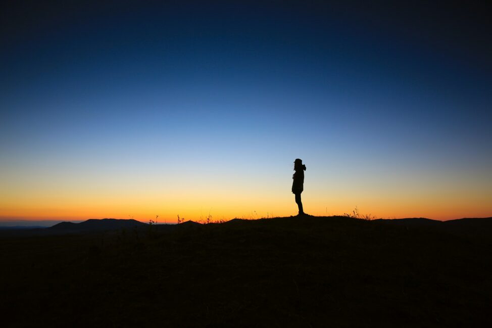 a person standing on the ground backlit by a blue yellow and orange sunrise - Face Your Fear